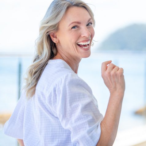 Beautiful mature woman portrait at waterfront house.  She is happy and smiling with the sea behind her. She looks relaxed and could be on vacation.